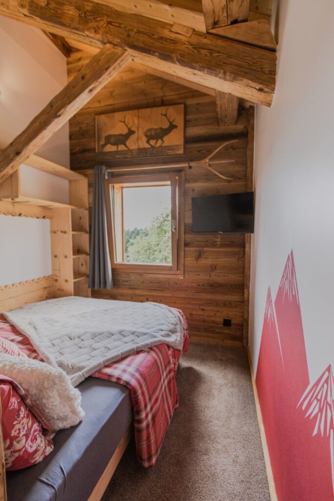 Chambre cosy : moquette confortable, charpente apparente, déco montagne rouge, vue nature