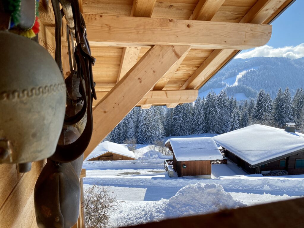 Vue du balcon, charpente massive, chalets enneigés, forêts lointaines sous la neige, panorama ensoleillé