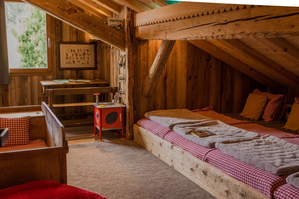 Chambre dortoir sous pente du toit : 4 lits alignés, longue tête de lit commune avec prises, poutre traversante, bureau d'enfants, lits bébé en bois