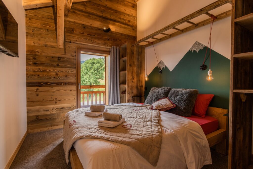Chambre double en suite, Appartement Rosalie - Tête de lit représentant des montagnes, vue sur la montagne depuis le balcon, lit soigneusement préparé avec serviettes, oreillers moelleux et coussins en peau de mouton