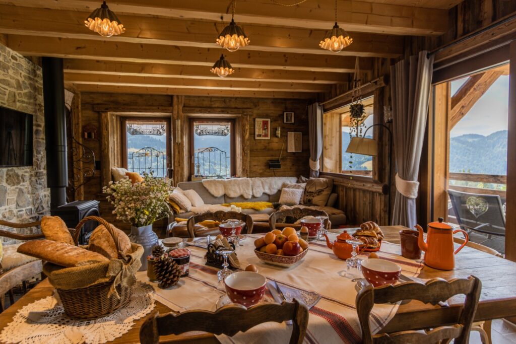 Table dressée pour le festin, vaisselle vintage, vue par la baie sur montagnes et forêts, ambiance chaleureuse du salon