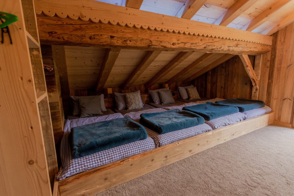 Chambre dortoir sous la pente du toit, 4 lits alignés, tête de lit commune avec prises et commandes, magnifique poutre traversante