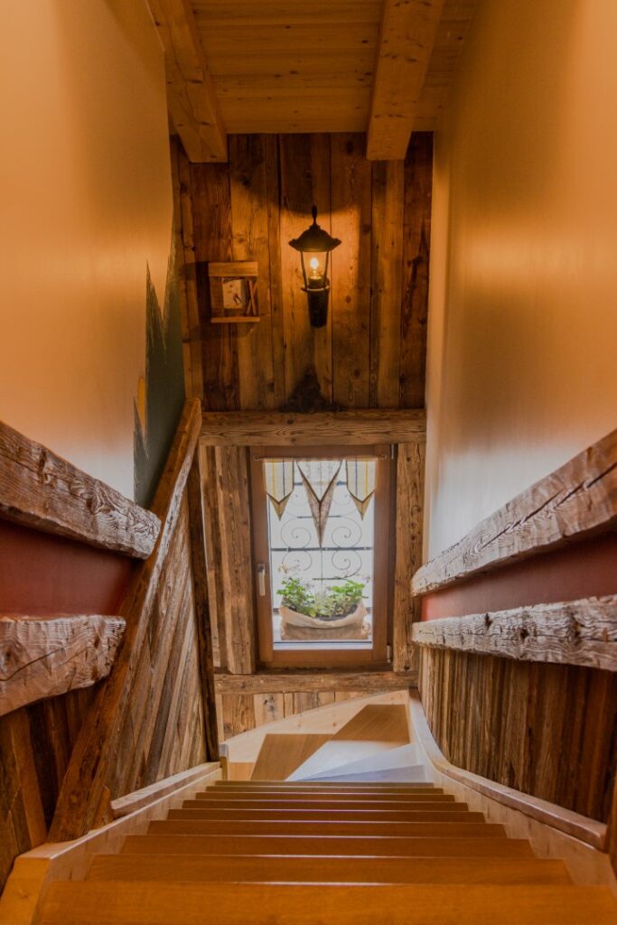 Escalier avec vue fenêtre, structure fer forgé, plante verte, vieux bois, tons rouge et vert, style montagne