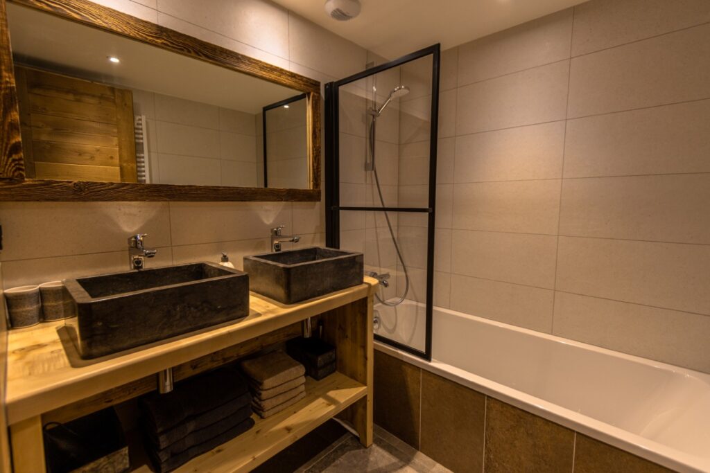 Salle de bain double vasque en pierre naturelle, baignoire, cadre noir effet atelier, plan bois massif